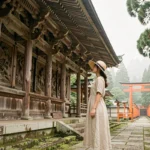 Voyageuse devant un temple bouddhiste de Kyoto entouré de torii vermillons et de cèdres centenaires au Japon